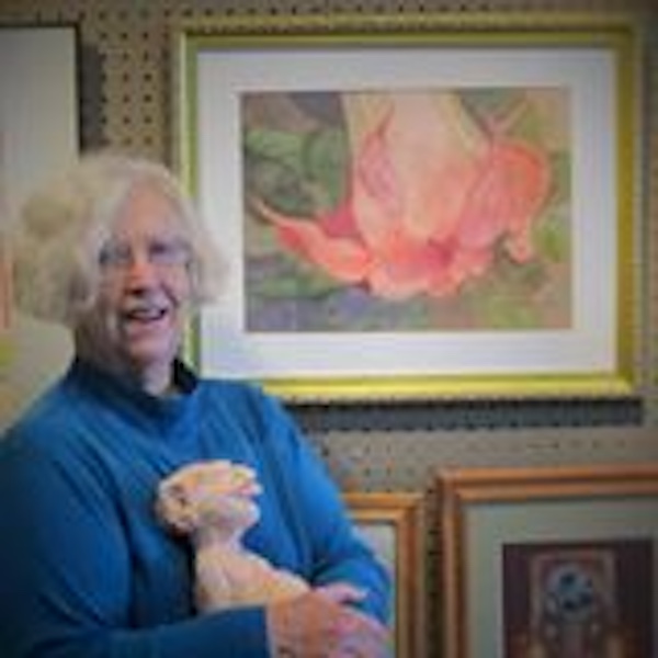 Artist Aline McCracken in front of a watercolor flower painting. Aline is wearing a blue top and is holding a stuffed animal.