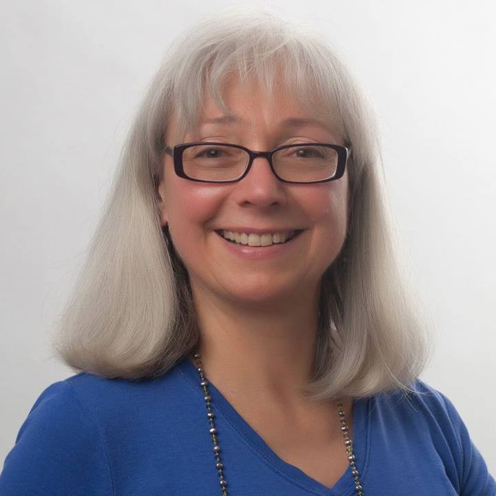 A smiling Karen Barker wearing black-rimmed eyeglasses and a blue blouse.