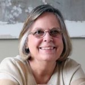 A smiling Merry Anne McSpadden wearing glasses and a beige top.